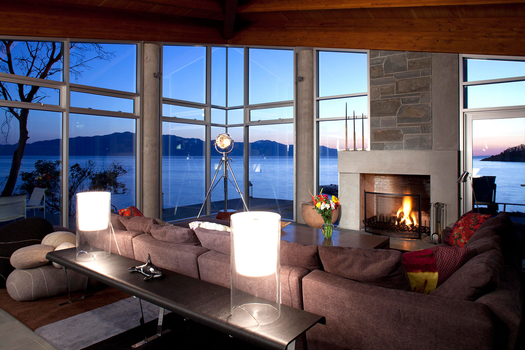 Living room at dusk — fireplace, deep sofas and a panoramic sea view